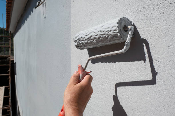 painter's hand holding a roller filled with paint to paint an exterior wall